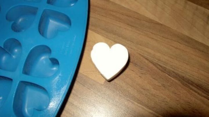 Ein herzf&ouml;rmiger, wei&szlig;er Gegenstand liegt neben einer blauen Silikonform mit Herzf&ouml;rmigen Vertiefungen auf einer Holzoberfl&auml;che.