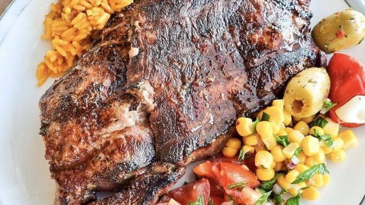 Ein saftiges Grillsteak liegt auf einem Teller, umgeben von gew&uuml;rztem Reis und frischem Gem&uuml;se, ideal f&uuml;r ein Grillfest.