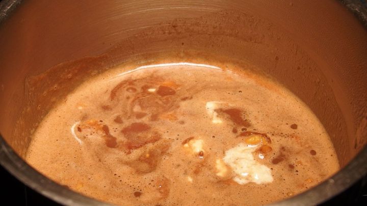 Eine schokoladige Sauce kocht in einem Topf, umgeben von gl&auml;nzendem Metall und einem warmen, einladenden Ambiente.