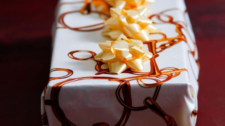 Ein h&uuml;bsch verpacktes Geschenk in T&uuml;cher, geschm&uuml;ckt mit einer dekorativen Schleife, liegt auf einem Holztisch.