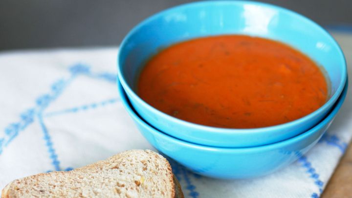 Eine blaue Sch&uuml;ssel mit roter Suppe steht auf einem Tisch, daneben liegt ein St&uuml;ck Brot, ideal f&uuml;r eine Mahlzeit.