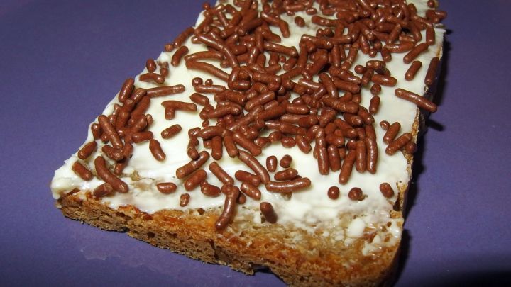 Ein St&uuml;ck s&uuml;&szlig;es Brot mit einer cremigen Schicht und Schokoladenstreuseln darauf liegt auf einem lila Teller.