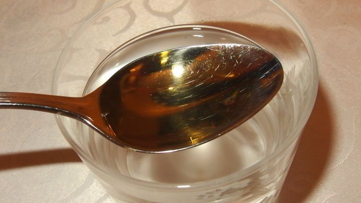 Ein L&ouml;ffel liegt auf einem Glas Wasser, bereit zur Zubereitung des Apfelessig-Tranks am Morgen.