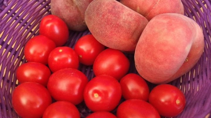 Rote Tomaten und Pfirsiche liegen in einem lila Korb und symbolisieren g&uuml;nstige, frische Lebensmittel zum Geld sparen.