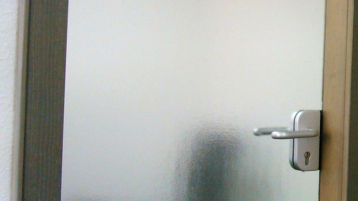 Eine Glast&uuml;r mit Struktur befindet sich im Fokus, w&auml;hrend sie gereinigt wird. Der Hintergrund bleibt unscharf.