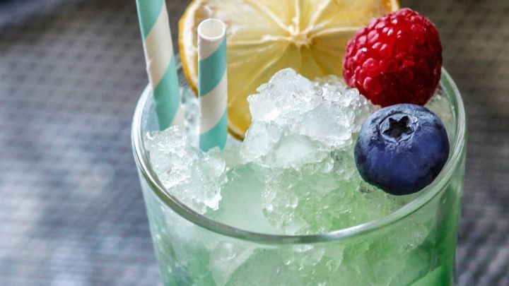 Ein Getr&auml;nk aus crushed Eis im Glas mit frischen Beeren und einer Zitrone dekoriert, auf einer dunklen Oberfl&auml;che.