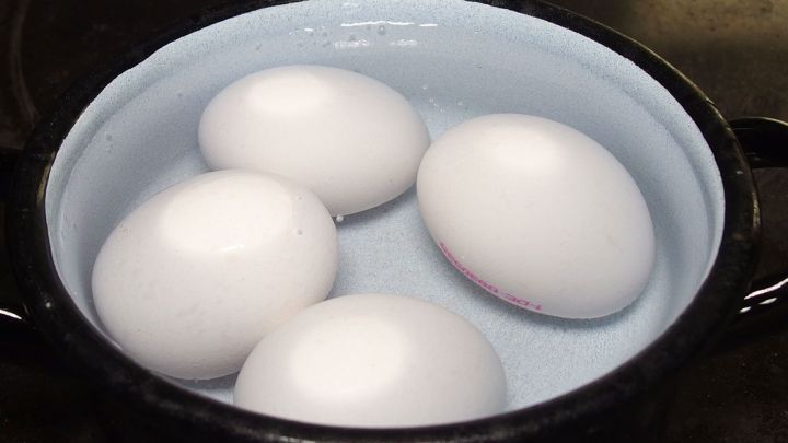 Vier wei&szlig;e Eier liegen in einem Topf mit Wasser, w&auml;hrend sie gekocht werden, um ein perfektes Fr&uuml;hst&uuml;cksei zuzubereiten.