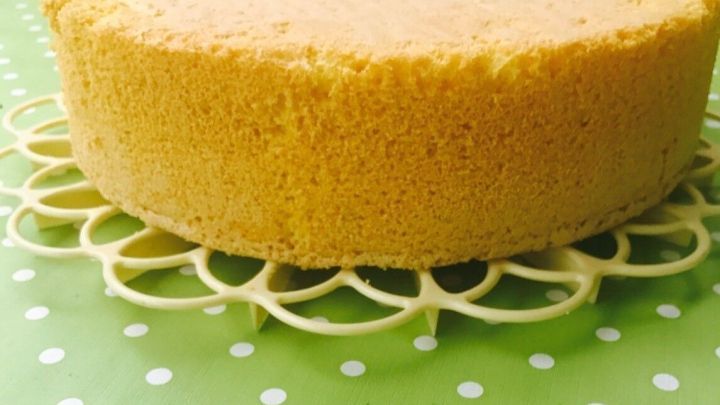 Ein luftiger Biskuitkuchen steht auf einem dekorativen Teller und liegt auf einer gr&uuml;nen Tischdecke mit Punkten.