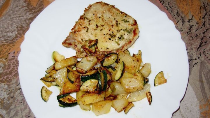 Gegrilltes Brot liegt neben einer bunten Mischung aus Backofengem&uuml;se auf einem wei&szlig;en Teller, umgeben von einem schlichten Tischdeckenmuster.