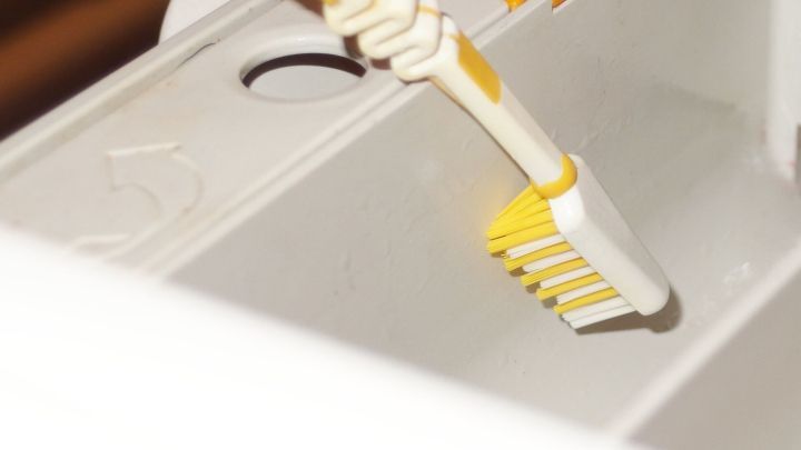Eine Zahnb&uuml;rste reinigt das Waschpulverfach in einer Waschmaschine, um R&uuml;ckst&auml;nde zu entfernen und Hygiene zu gew&auml;hrleisten.