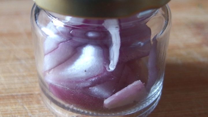 Ein kleines Glasgef&auml;&szlig; mit geschnittenen Zwiebeln, das auf einer Holzoberfl&auml;che steht, erzeugt einen Zwiebelgeruch.
