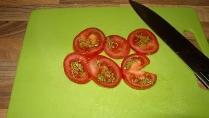 Auf einem gr&uuml;nen Schneidebrett liegen frisch geschnittene Tomaten, w&auml;hrend ein K&uuml;chenmesser daneben platziert ist.