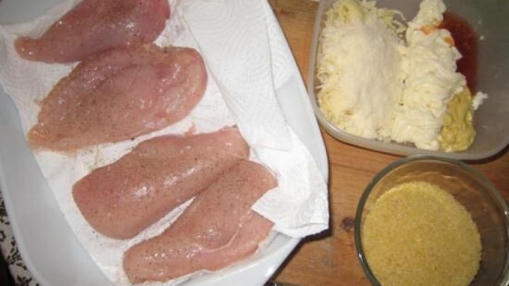 Gebackene H&uuml;hnerbrustfilets liegen auf einem K&uuml;chentuch, umgeben von K&auml;se und Gew&uuml;rzen in Schalen.