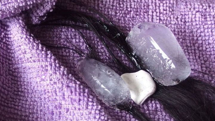 Haarstr&auml;hnen sind mit Eisw&uuml;rfeln umwickelt, w&auml;hrend sie auf einem lila Tuch liegen und eine experimentelle Mischung bilden.
