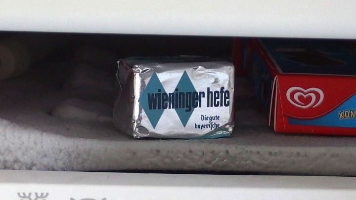 Ein Block frischer Hefe liegt eingefroren im Gefrierfach zwischen anderen Lebensmitteln.