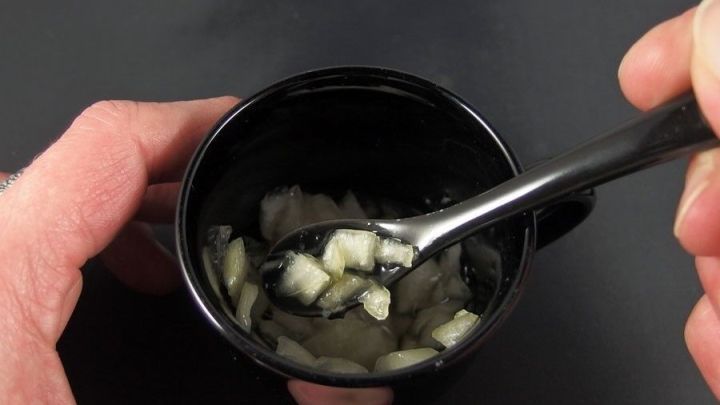 In einer schwarzen Tasse wird ein Hustenmittel aus Zwiebelst&uuml;cken mit einem L&ouml;ffel verr&uuml;hrt.