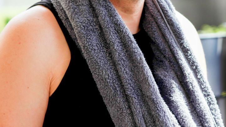 Ein Mann tr&auml;gt ein graues Handtuch um den Hals, w&auml;hrend er sich in der warmen Sonne entspannt und die Umgebung betrachtet.