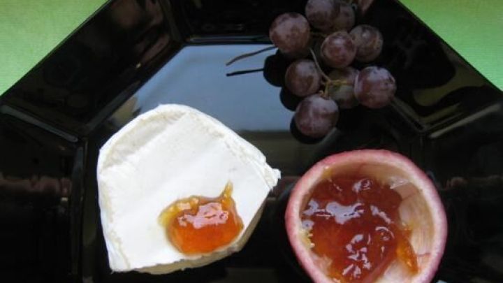 Zwei K&auml;se St&uuml;cke auf einem schwarzen Teller, einer mit Orangenmarmelade und frischen Trauben daneben.