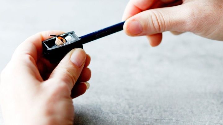 Ein Hand greift einen Eyelinerstift und spitzt ihn vorsichtig in einem Anspitzer auf einer hellen Oberfl&auml;che an.