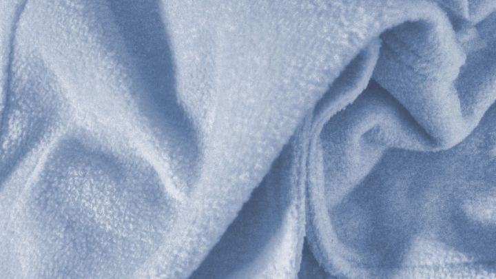 Eine blaue Decke liegt zerknittert auf einer Oberfl&auml;che und zeigt eine glatte Textur, die zur Entfernung von Schimmelflecken einl&auml;dt.