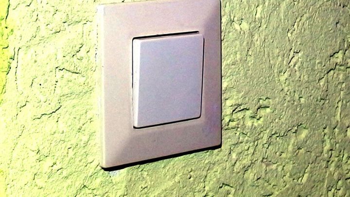 Ein Lichtschalter an einer strukturierten gr&uuml;nen Wand wartet darauf, gereinigt zu werden, um seine Vergilbung zu entfernen.