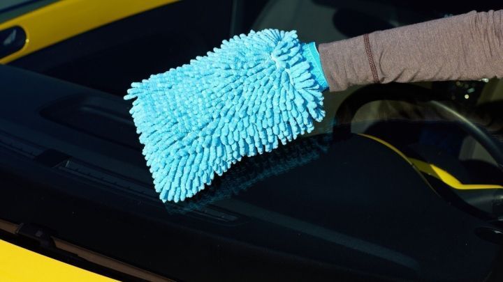 Ein blauer Reinigungsschwamm wird verwendet, um einen Kratzer von der Autoscheibe eines gelben Fahrzeugs zu entfernen.