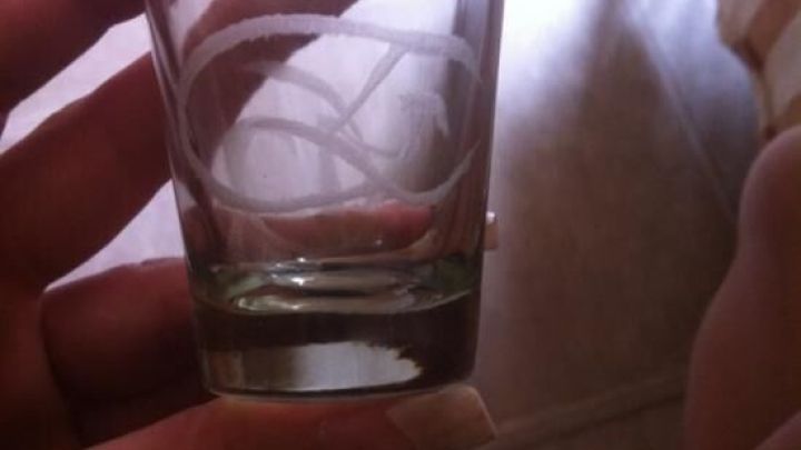 Ein graviertes Glas wird von einer Hand gehalten, im Hintergrund ist ein helles Zimmer mit einem Stuhl sichtbar.