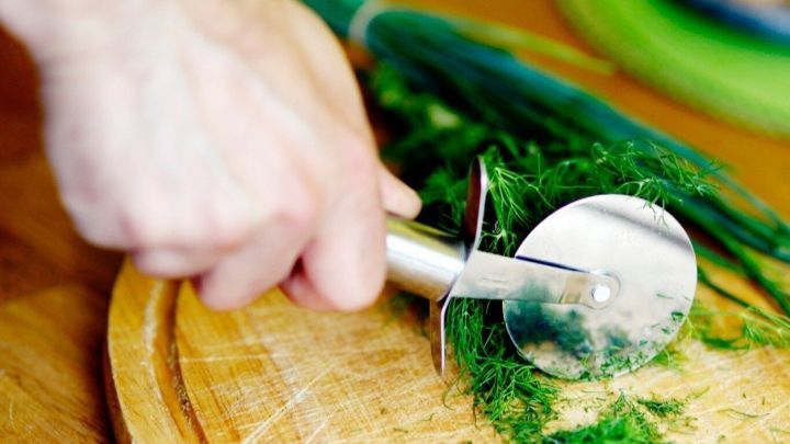 Ein Pizzaschneider schneidet frische Kr&auml;uter auf einem Holzbrett in einer modernen K&uuml;che.