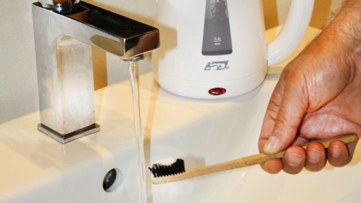 Eine Hand h&auml;lt eine Zahnb&uuml;rste unter flie&szlig;endem Wasser am Waschbecken, um Energiekosten beim Z&auml;hneputzen zu sparen.