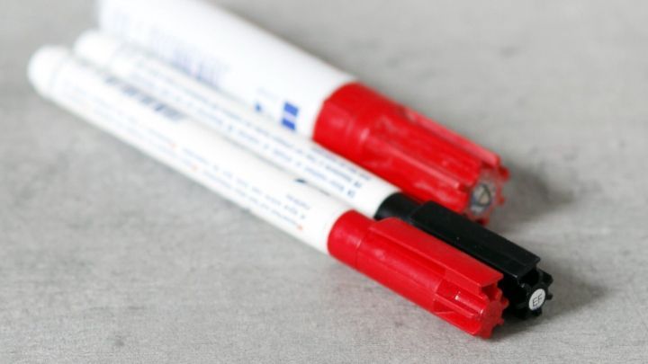 Mehrere Edding-Stifte liegen auf einer grauen Oberfl&auml;che. Zwei Kappen sind rot, eine ist schwarz, alle Stifte sind wei&szlig;.