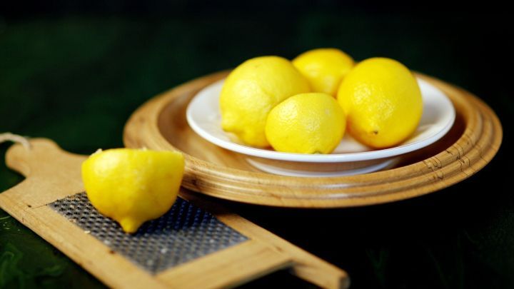 Frische Zitronen auf einem Teller neben einer Reibe, ideal f&uuml;r Geruchstilgung mit Zitronenessig in der K&uuml;che.