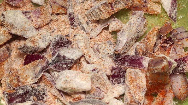 Kross gebratene R&ouml;stzwiebeln liegen in einer gr&uuml;nen Sch&uuml;ssel, umgeben von einer Mischung aus Gew&uuml;rzen und Zwiebelst&uuml;cken.