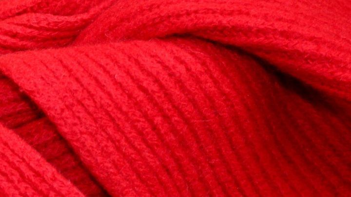Ein rotes Wollst&uuml;ck liegt sanft gefaltet auf einem Tisch, bereit zum Gl&auml;tten oder Aufrebbeln f&uuml;r ein Strickprojekt.