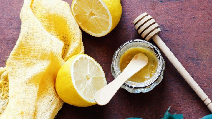 Zwei halbierte Zitronen liegen neben einem Glas mit Honig und einem Holzl&ouml;ffel auf einem rustikalen Tisch, um eine erfrischende Gesichtsmaske zuzubereiten.