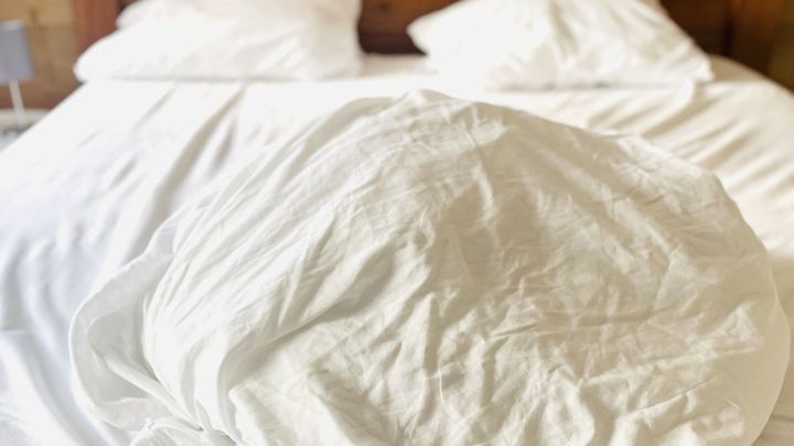 Ein Bett mit frisch gewaschenen, wei&szlig;en Bettlaken zeigt, dass es bereit ist f&uuml;r das Bettenbeziehen in einem Holzraum.