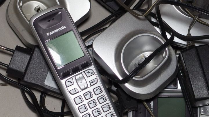 Ein &auml;lteres schnurloses Telefon liegt umgeben von Ladestationen und Kabeln, die ineinander verwickelt sind.