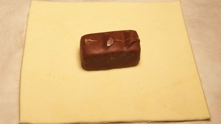 Ein St&uuml;ck Bl&auml;tterteig liegt auf einer Arbeitsfl&auml;che, w&auml;hrend ein Schokoladenst&uuml;ck darauf platziert ist, bereit zum Falten.