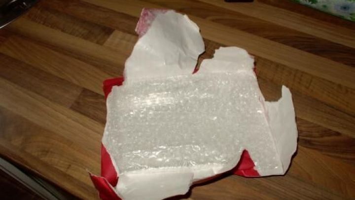 Ein zerknittertes St&uuml;ck Luftpolsterumschlag liegt auf einer Holzoberfl&auml;che und ist teilweise offen, bereit zur Wiederverwendung.