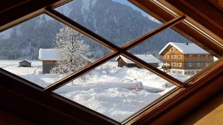 Ein Fenster zeigt eine verschneite Landschaft mit einem Haus und B&auml;umen. Umgezogen, jedoch ohne Sichtschutz am Fenster.
