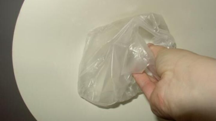 Eine Hand h&auml;lt eine durchsichtige T&uuml;te, die anscheinend eine Energiesparlampe enth&auml;lt, w&auml;hrend sie sich &uuml;ber einem Tisch befindet.