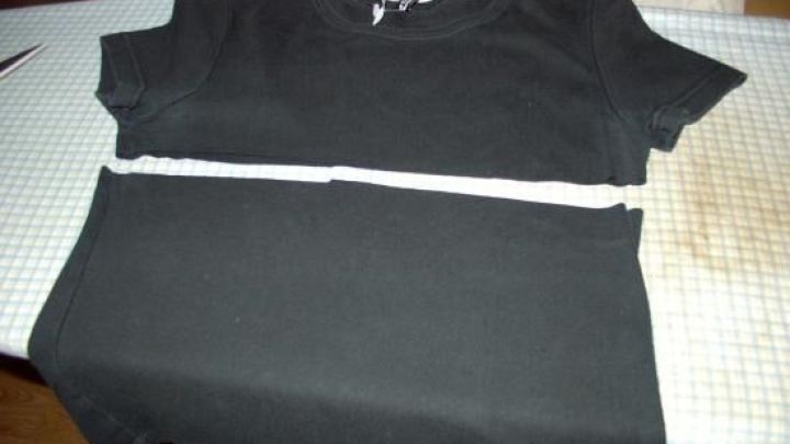 Ein schwarzes Shirt liegt auf einem Tisch, w&auml;hrend es in der Mitte mit einem wei&szlig;en Band zum kreativen Verl&auml;ngern markiert ist.