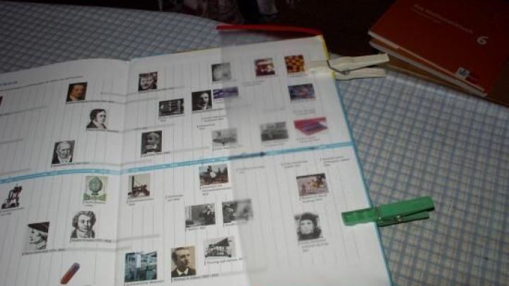 Ein Schulbuch liegt ge&ouml;ffnet auf einem Tisch und zeigt Bilder von historischen Pers&ouml;nlichkeiten, erg&auml;nzt durch handschriftliche Notizen.