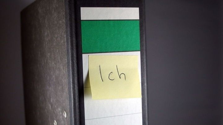 Ein Ordner steht aufrecht und zeigt farbige Register, darunter ein gelber Zettel mit "Ich", der wichtige Unterlagen kennzeichnet.