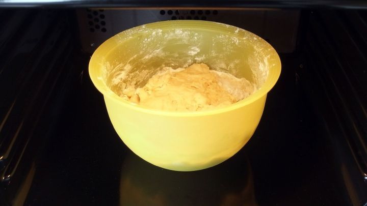 Ein gelbes Sch&uuml;sselchen mit Hefeteig geht in der Mikrowelle. Der Teig ist luftig und befindet sich auf einem Rost in der Mikrowelle.