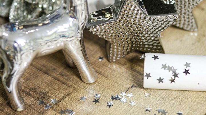 Silberner Hirsch und glitzernde Stern-Deko auf Holztisch, umgeben von verstreutem Sternkonfetti, neben Kleberoller.