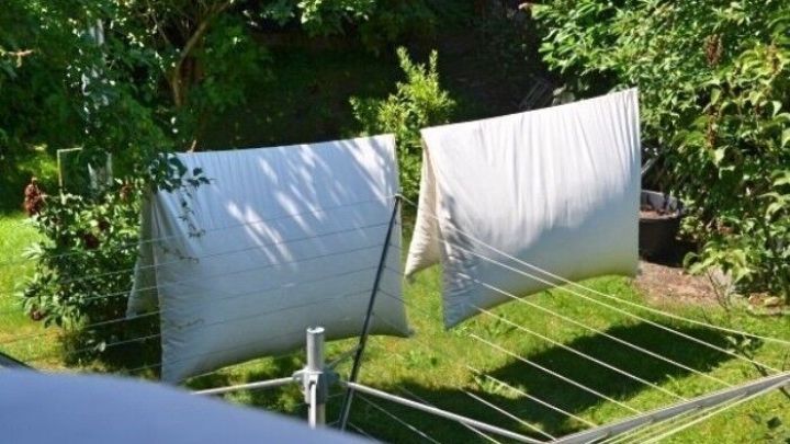 Wei&szlig;e Bettw&auml;sche h&auml;ngt frisch gewaschen auf einer W&auml;scheleine im Garten, um in der Sonne zu trocknen.