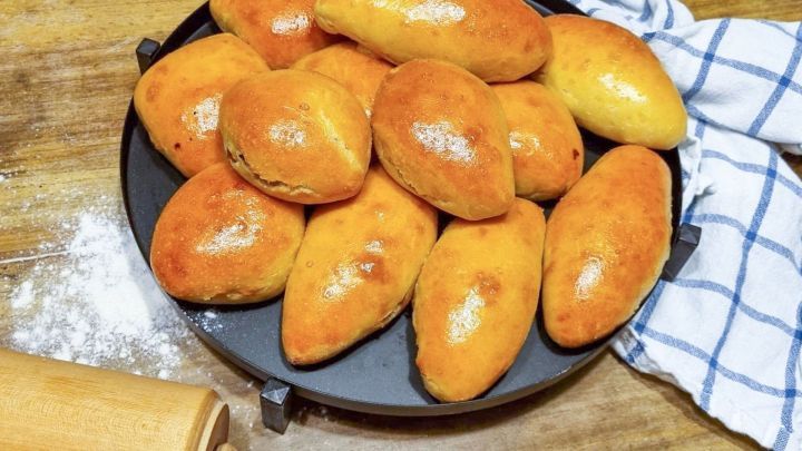 Auf einem schwarzen Teller liegen frisch gebackene, goldbraun gl&auml;nzende Geb&auml;cke ohne Hefe, umgeben von einer Holzoberfl&auml;che und einem Nudelholz.