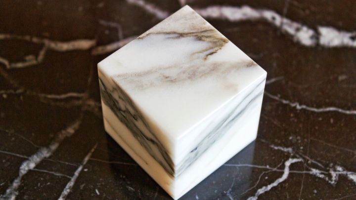 Ein stumpfer Marmorblock steht auf einer dunklen, marmorierten Fl&auml;che und hebt sich durch seine glatte, reflektierende Oberfl&auml;che ab.