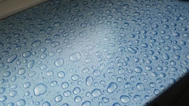 Wassertropfen liegen auf einer blauen Fensterbank, die eine erneuerte, frische Oberfl&auml;che zeigt und die Feuchtigkeit hervorhebt.