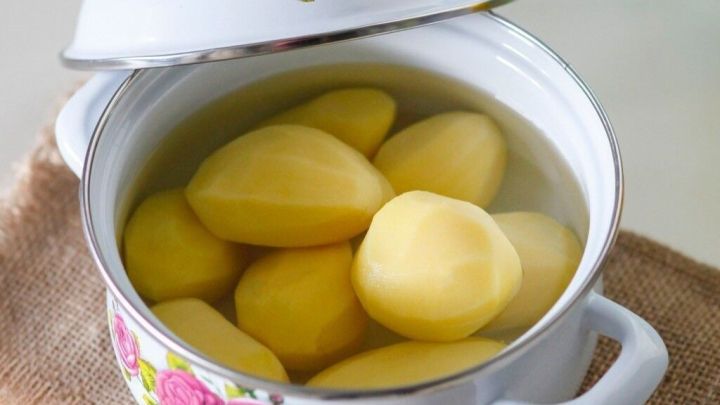 Kartoffeln liegen in einem dekorativen Topf mit Wasser, der auf einem rustikalen Tisch steht, bereit zum Kochen.